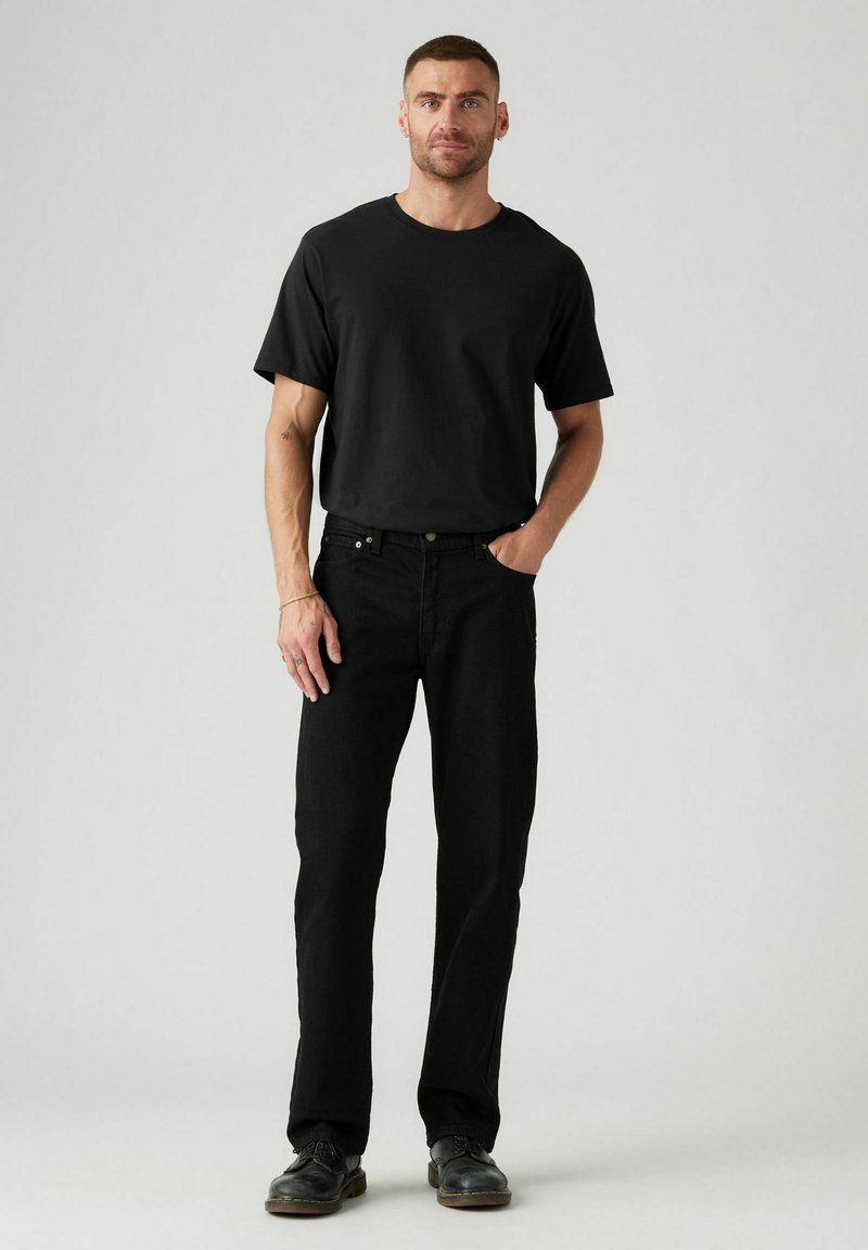 T-shirt nera a maniche corte abbinata a jeans neri a gamba dritta. Il tessuto di cotone presenta una texture liscia, completando un look monocromatico.