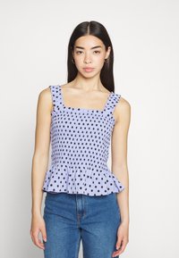 Top peplum em lilás com bolinhas pretas, decote quadrado e alças com babados. Feito de um tecido texturizado com um corpete justo.