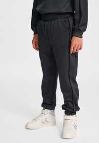Mörkgrå sweatpants med elastisk midja, två sidofickor och en subtil logotyp. Matchas med vita högkängor.