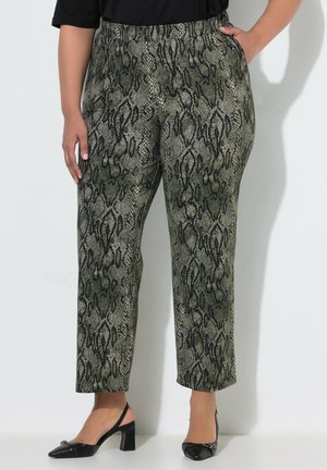 Kvinde iført højtaljede bukser med grøn- og sort slangeprint, elastisk talje og sorte slingback blokhæle.