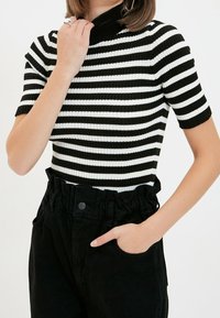 Haut à rayures noir et blanc, en ribbed, avec un col montant et des manches courtes, associé à un pantalon noir taille haute avec une ceinture froncée.