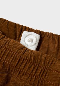 Taille en velours côtelé marron élastiquée avec un bouton blanc ajustable attaché à une languette en tissu pour le réglage de la taille.