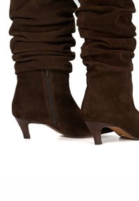 Brown suede slouchy ankle boots with a tapered heel and side zipper. The texture is soft with gathered detailing around the upper.