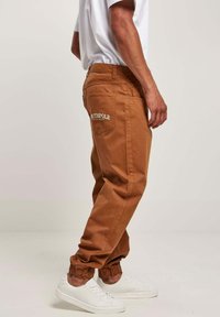 Tan cargo-bukser med elastiske manchetter, der har sidelommer og en baglomme med hvid "SOUTHPole" logo broderi. Stylet med hvide sneakers.