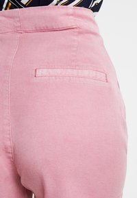 Różowe spodnie dżinsowe z tylnią kieszenią ze prostym szwem. Tkanina ma gładką teksturę z delikatnym połyskiem.