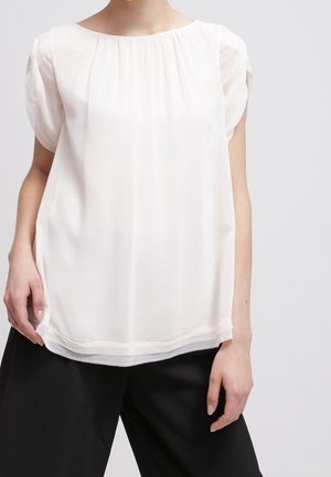 Blusa leggera, trasparente, di colore crema, con scollo rotondo e maniche corte a palloncino, caratterizzata da una leggera arricciatura allo scollo.