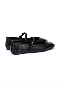Bailarinas de cuero negro con punta afilada, acentos de tachuelas brillantes y una correa con un hebilla plateada. Textura suave y diseño minimalista.