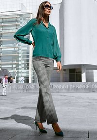 Tee-farbene Bluse mit Knöpfen, schwarz-weiße gemusterte Schlaghose und tee-farbene High Heels. Glattes Material und strukturierter Schnitt mit übergroßen Sonnenbrillen.
