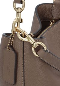 Bruine leren handtas met een textuur oppervlak, gouden hardware accenten, een afneembare schouderband en een label met reliëfbranding.