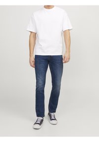 Vit bomullströja med rund halsringning, ihopparad med mörkblå jeans och marinblå sneakers med vita sulor och snören.