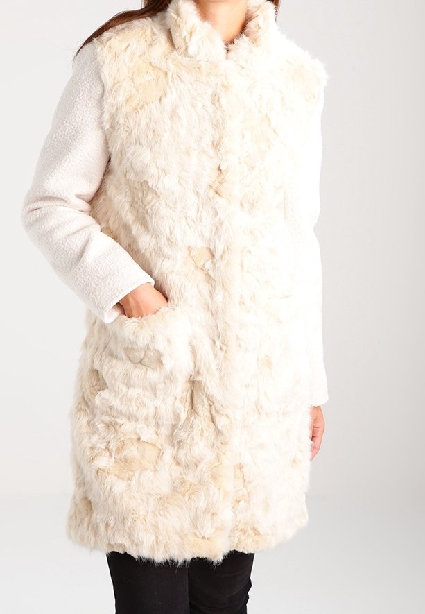 Faux-Fur-Mantel in Creme mit strukturiertem Körper, weißen Ärmeln, hohem Kragen und Seitentaschen. Weiche Oberfläche mit unterschiedlichen Fellmustern.