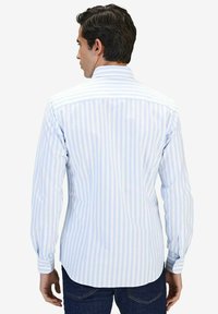 Pitkähihaisa paita, jossa on vaaleansinisiä ja valkoisia pystysuoria raitoja, napitettava kaulus ja pyöreä helma. Kankaan pinta näyttää sileältä ja napakalta.