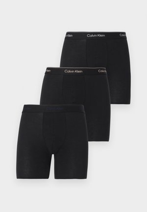 Tre svarte Calvin Klein boxershorts med merkede midjebånd i forskjellige nyanser av svart, stablet i en forskjøvet rekkefølge.