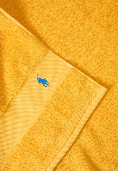 Λαμπερή κίτρινη πετσέτα με υφασμένη μπορντούρα και μικρό μπλε κεντημένο λογότυπο ενός ανθρώπου που παίζει πόλο.