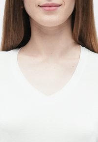 Λευκό T-shirt με λαιμόκοψη σε σχήμα V και ομαλή υφή, με κοντά μανίκια και διακριτική λεπτομέρεια λογότυπου κοντά στη γραμμή του λαιμού.