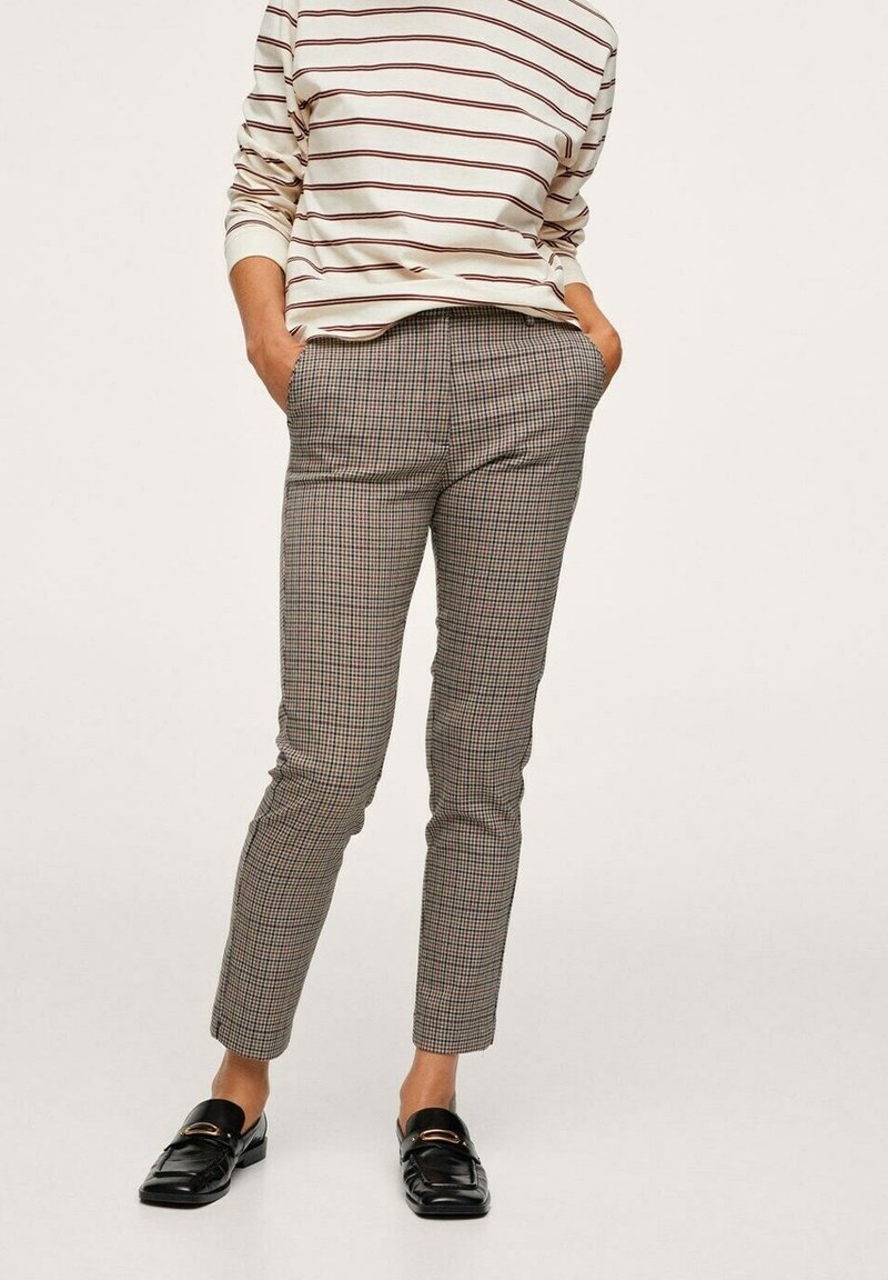 Personne portant un pantalon slim à carreaux, les mains dans les poches, associé à des mocassins noirs et un haut rayé à manches longues.