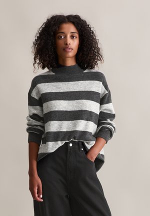 Grijze en zwarte gestreepte trui met een hoge halslijn en opgerolde mouwen, gecombineerd met hoge zwart taille broek, die een ontspannen pasvorm toont.