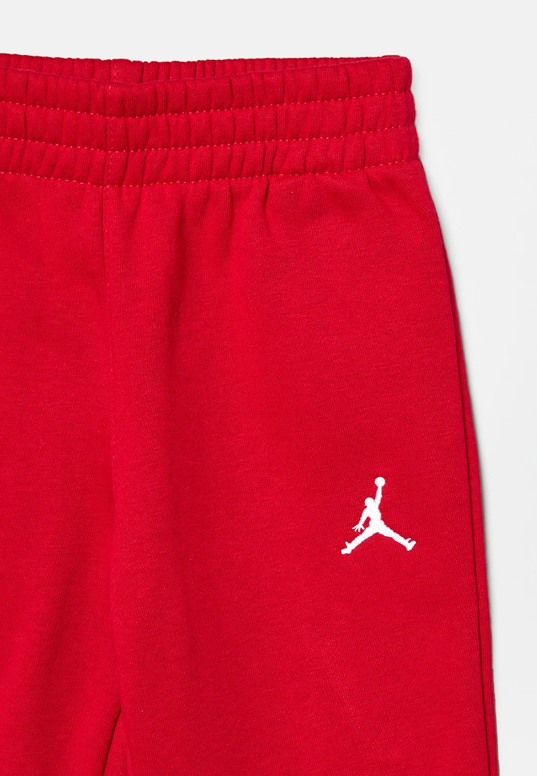 Rote Baumwoll-Sweatpants mit einem elastischen Bund und einem weißen Jordan-Logo, das am unteren Bein gestickt ist. Glatte Textur.