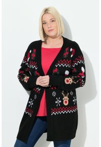 Schwarze Strickjacke mit Feiertagsmotiven, darunter Rehe, Schneeflocken und rote Akzente. Offene Front, gerippte Bündchen und Saum.