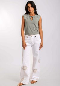 Top corto de color verde claro con escote en forma de ojal. Pantalones anchos blancos con bordados florales. Modelo con sandalias planas.