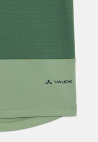Zelené tričko z texturované látky, se světle zeleným lemem a modrým logem "Vaude" v pravém dolním rohu.