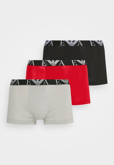 Tres pares de calzoncillos tipo boxer: gris, rojo y negro, cada uno con una cinturilla negra que presenta un logo blanco y una tela suave y elástica.