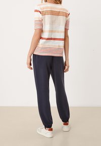 Camiseta a rayas en crema, naranja y rojo. Pantalones sueltos azul marino con cintura elástica. Zapatillas blancas con detalles naranjas.