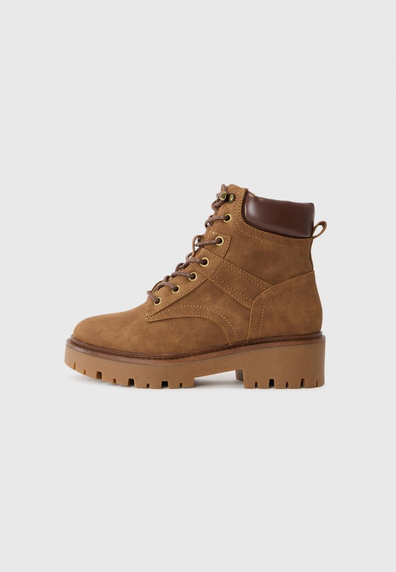Bottes chelsea en suede marron avec une finition texturée, bout rond et accents en cuir marron. Comprend des lacets, des œillets en métal et une épaisse semelle en caoutchouc.
