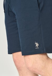 Pantaloni corti in cotone blu navy con vita regolabile tramite cordino e un piccolo logo USPA bianco. Texture liscia con taglio di lunghezza media.