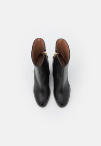 Botas de tobillo de cuero negro con textura suave, punta redondeada y detalles de cremallera dorada en los laterales. Interior forrado con material marrón.