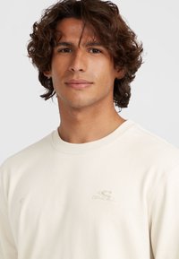 Lichtbeige sweatshirt met een ronde hals en geribbelde manchetten. Bevat een subtiele geborduurde logo op de borst, met een gladde stofstructuur.