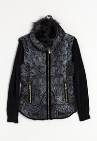 Veste noire avec un motif paisley à l'avant, fermetures éclair dorées, manches tricotées et un col en fourrure duveteux suspendue à un cintre noir.
