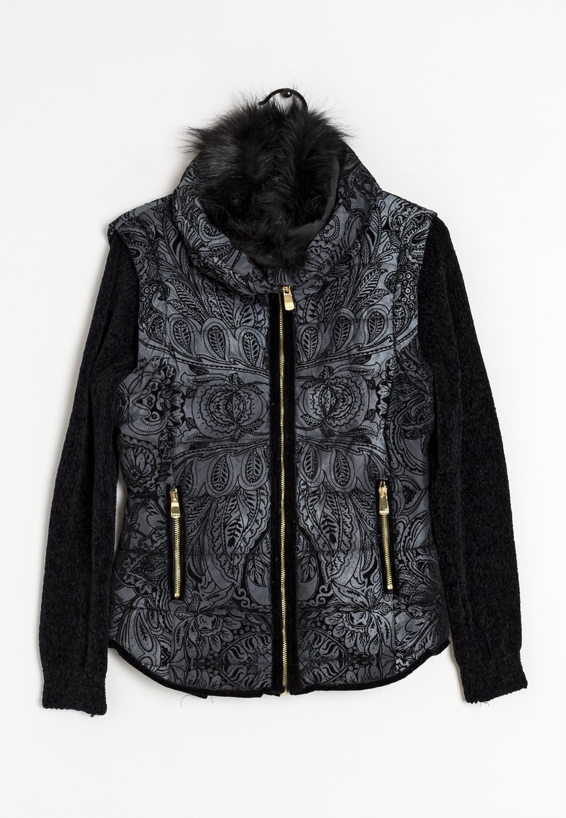 Veste noire avec un motif paisley à l'avant, fermetures éclair dorées, manches tricotées et un col en fourrure duveteux suspendue à un cintre noir.