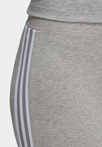 Leggings atletici grigi realizzati in un morbido mix di cotone, con tre strisce bianche verticali lungo il lato per un contrasto e uno stile distintivi.