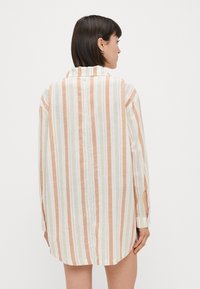 Langarmshirt met verticale strepen in oranje en gebroken wit. Gemaakt van een lichtgewicht stof, met een kraag en knoopsluitingen op de manchetten.