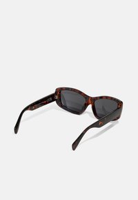 Gafas de sol carey con un diseño elegante de ojo de gato, lentes grises y patillas negras con una textura brillante y un patrón sutil.