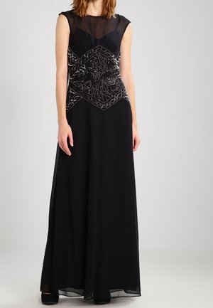 Woman wearing a sleeveless black floor-length gown with sheer top and intricate beadwork floral design on the bodice.