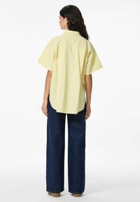 Geel-witte gestreepte shirt met korte mouwen en rugpas, met een gebogen zoom, gedragen met wijde donkerdenim broek.