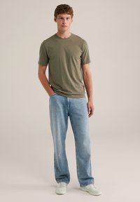 Camiseta de manga corta verde oliva combinada con jeans rectos azul claro y zapatillas blancas, presentada sobre un fondo neutro.
