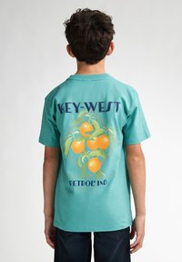 Tyrkysové bavlněné tričko s grafikou pomerančů a textem "KEY-WEST PETROL IND" na zadní straně. Kulatý výstřih, krátké rukávy.