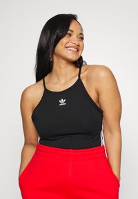 Top sportivo nero con spalline sottili, con un logo Adidas bianco. Abbinato a pantaloni tuta rossi, che mostrano una vestibilità comoda.