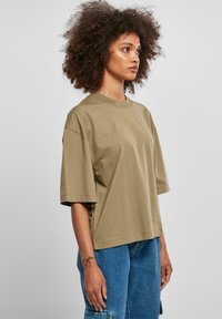 Khaki oversized tričko vyrobené z bavlny. Má krátké rukávy a kulatý výstřih, s hladkou texturou a uvolněným střihem.