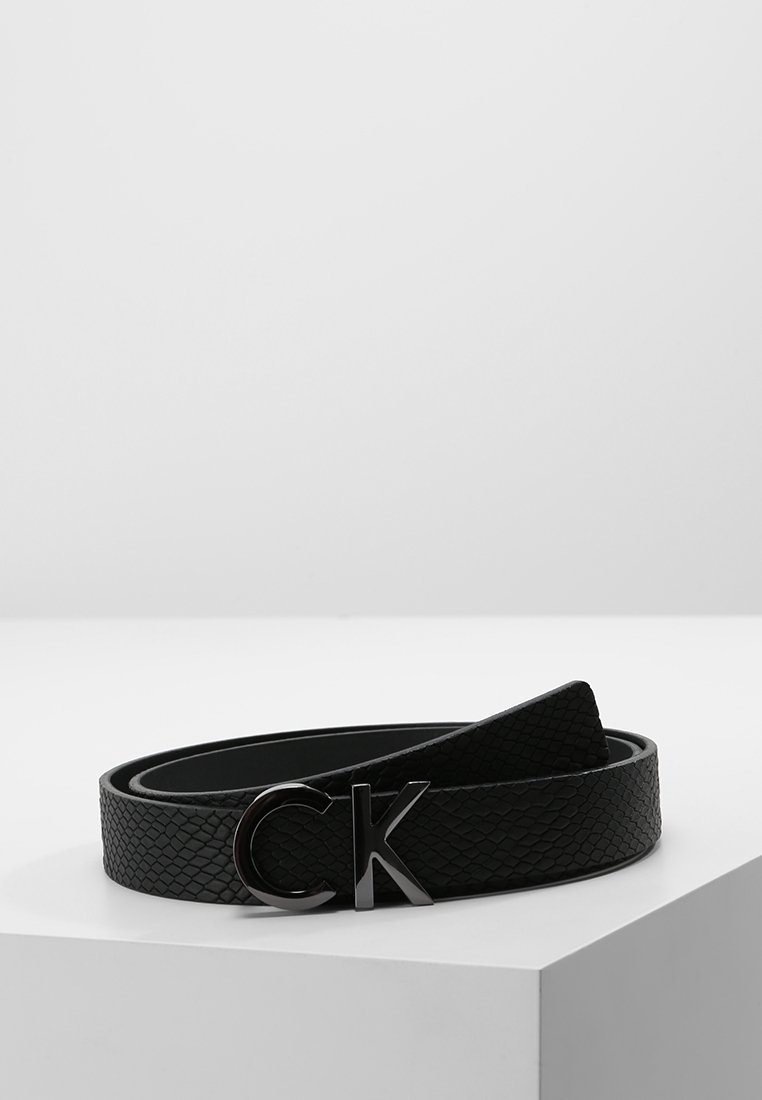 Ceinture en cuir texturé noir enroulée sur une surface blanche avec une boucle glacée noire portant le logo « CK ».