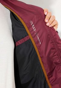 Bordeaux en zwarte jack interieur met een gladde, waterafstotende stof, contrasterend oranje chevronpatroon en een zichtbaar merlabel.