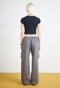 Černé zkrácené tričko spárované s volnými šedými cargo kalhotami, které mají boční kapsy, elastický pas a široké nohavice. Jednoduché barvy, hladká textura.