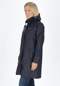Granatowy, wodoodporny płaszcz przeciwdeszczowy z kapturem, z zapięciem na guziki z przodu, bocznymi kieszeniami oraz regulowanym sznurkiem przy szyi.