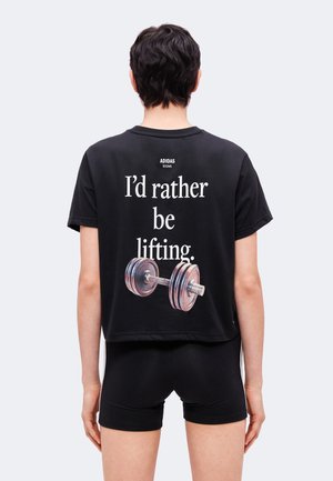 Person trägt ein schwarzes Adidas-Shirt mit dem Text "I'd rather be lifting" und einem Bild einer Hantel auf dem Rücken, kombiniert mit schwarzen Shorts.