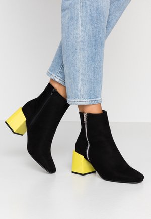 Bottines en daim noir avec talons carrés jaunes, dotées d'une fermeture éclair latérale et d'une pointe effilée. Conçues pour un look élégant et contemporain.