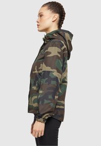 Roheline ja pruun camo jakk, millel on kapuuts, tõmblukk ja elastsed mansetid. Kerge, tekstuurse kangaga.