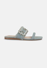 Sandal in denim blu con una cinturino frangiato decorato con una grande fibbia simile a un gioiello, accentuato da una soletta testurizzata e suola piatta.